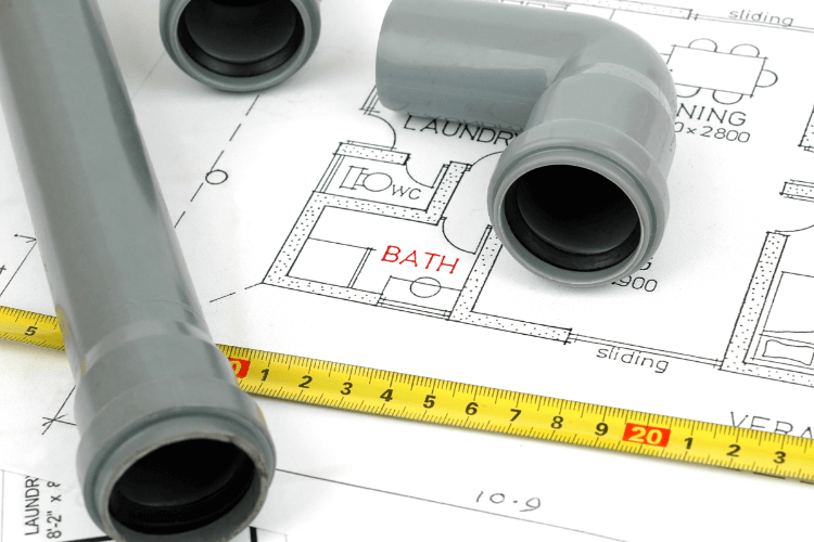 Multiple pipe pieces laid out on a bathroom plan map and next to a ruler
